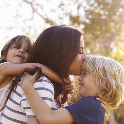 Mother Carrying Son And Daughter As They Play In Park